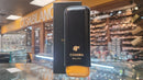 A black and yellow leather cigar pouch with the Cohiba brand logo, displayed on a glass shelf in a store with various items in the background.
