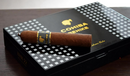 A Cohiba Behike 54 cigar resting on top of its black and gold patterned box.
