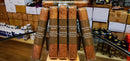 Five wrapped bars of chocolate arranged upright on a wooden display stand inside a store. The wrappers are brown with white text reading 'Olive Serie C 43x50' and 'Handmade Tabacaria de Nicargagua.