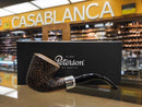 A Peterson smoking pipe with a dark brown speckled bowl and black stem, displayed in front of its black branded box on a reflective surface inside a store, with a large yellow 'CASABLANCA' sign in the background.