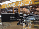 A dark brown smoking pipe with a textured bowl and long stem, displayed on a clear stand in front of its black Peterson box. The background shows a blurred retail shop interior with a prominent yellow 'CASABLANCA' sign.