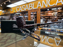 A Peter Taylor handcrafted smoking pipe with a dark wood bowl and long stem, displayed on a clear stand in front of a black branded box inside what appears to be a retail shop, with a blurred background showing a large 'CASABLANCA' sign.