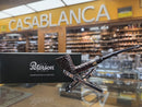 A Peterson smoking pipe displayed on a stand in front of its black branded box, with a blurred retail shop interior and a large 'CASABLANCA' sign in the background.