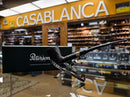 A black textured smoking pipe displayed on a clear stand next to a black Peterson box, set in a retail store with a blurred background and a yellow 'CASABLANCA' sign.