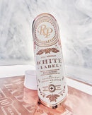 A white Connecticut Shade Wrapper 10-year vintage-style label bottle with rose gold metallic accents, standing upright on a reflective surface with a marble background.