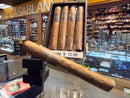 Cigar display with a large cigar in front and smaller cigars in a box, set against a store background.

