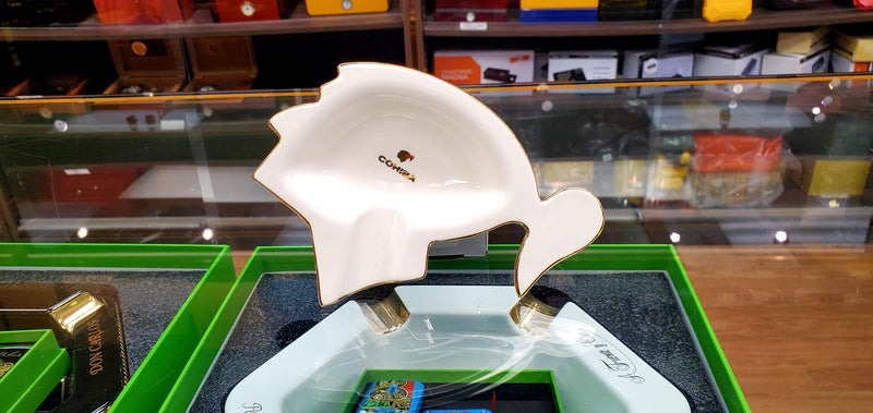 A white ashtray with a cohiba logo on it, displayed on a green surface in a store.