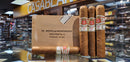 A box of Hoyo De Monterrey cigars, with individual cigars placed outside the box. The background is a cigar store with various other cigars and accessories visible.