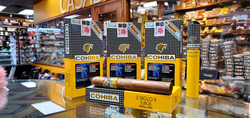 A pack of Cohiba Siglo 2 (Tubo) cigars displayed in a retail setting, with packaging that includes the brand name and the cigar's shape, size, and color information.
